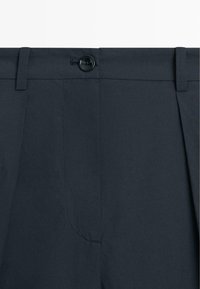 Mørkeblå skræddersyede bukser med bæltestropper, knaplukning og skjult lynlås foran i taljen.