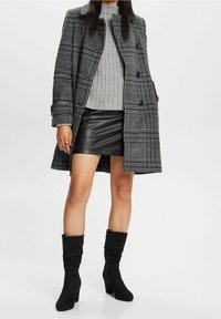 Harmaa ruudullinen päällysvaate, ribbattu harmaa neulepaita, musta nahkainen mini-hame ja mustat nilkkurit. Takissa on kaksipainikeellinen kiinnitys ja muodollinen muotoilu.