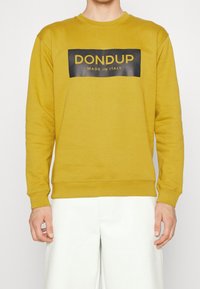 Żółta bluza z bawełny z okrągłym dekoltem i ściągaczami przy mankietach. Posiada czarny prostokątny grafik z napisem "DONDUP MADE IN ITALY."