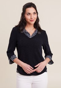 Top blu navy con maniche a tre quarti, caratterizzato da un colletto e polsini interni a fantasia; tessuto testurizzato, design a scollo a V, abbinato a pantaloni bianchi.