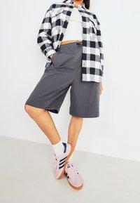 Black and white checked flannel shirt, gray shorts, pink sneakers with navy accents, white socks, model poses with one leg bent.