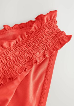 Parte inferior de bikini roja con un borde superior fruncido y suave, fabricada con un tejido elástico. El diseño enfatiza la textura y la elasticidad.