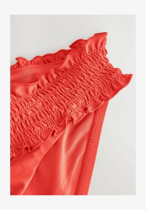 Pantaloni de baie roșii, cu un tiv plisat și un material neted, elastic. Designul subliniază textura și elasticitatea.
