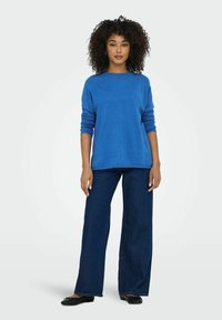 Blå stickad tröja med avslappnad passform, långa ärmar och ribbade manschetter, matchad med vida mörk denimjeans och svarta ballerinas.