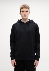 Μαύρο φούτερ από υφασμάτινο υλικό με υφή και διακριτό γεωμετρικό σχέδιο, διαθέτει μπροστινή τσέπη και κουκούλα με κορδόνι.