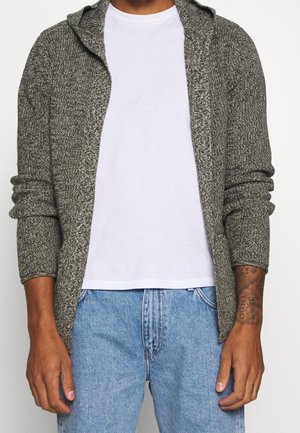 Cardigan grigio in maglia con cappuccio, aperto davanti e maniche lunghe, indossato sopra una t-shirt bianca, abbinato a jeans azzurri chiari.