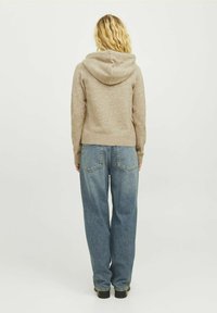 Felpa beige con scollatura sul retro, texture morbida e vestibilità comoda, abbinata a jeans blu a vita alta con tasche posteriori.
