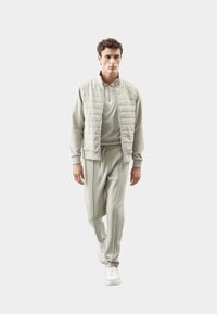 Gilet trapuntato verde chiaro sopra un pullover abbinato e pantaloni della tuta a gamba affusolata. Caratterizzato da chiusura con zip, vita con cordino e sneakers bianche.