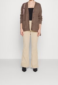 Brun ribbad cardigan med knappar, två framfickor, kombinerad med beiga utsvängda byxor och svarta klackstövlar. Enkel, avslappnad passform.