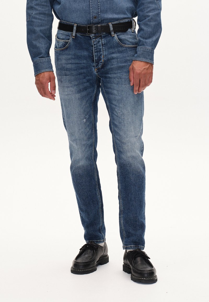 Jeans in denim blu medio con una vestibilità slim, caratterizzati da cuciture a contrasto, due tasche frontali e una cintura nera. Texture liscia.