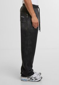Pantalones joggers de mezcla de algodón en gris oscuro con una cinturilla ajustada, bolsillo lateral y cierre con cordón. Textura suave con variación de color sutil.