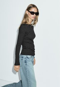 Zwart en grijs gestreept lang mouwen top, gecombineerd met lichtblauwe high-waisted jeans, die een slanke pasvorm en een zachte textuur tonen.