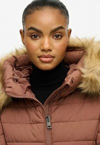 Brązowa pikowana kurtka z kapturem wykończonym futrem, z zamkiem z przodu i wysokim kołnierzem. Miękka tekstura z wzorem pikowania i ciemną warstwą podstawową.