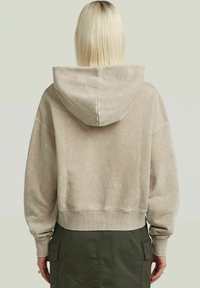 Hoodie beige accorciato in morbido tessuto con cappuccio regolabile, polsini e orlo a coste, caratterizzato da una leggera finitura testurizzata.