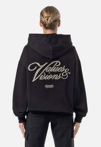 Felpa nera con cappuccio, caratterizzata da un testo audace e stilizzato "Values & Visions" in finitura oro metallico sul retro. Vestibilità morbida con polsini a coste.