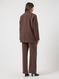 Καφέ κοστούμι με μακρύ σακάκι και παντελόνια φαρδιάς γραμμής. Λείο ύφασμα με δομημένους ώμους και μία τσάκιση στο πίσω μέρος.