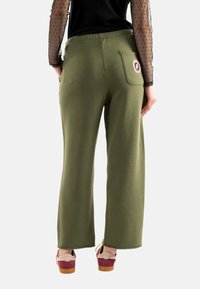 Pantalones de pierna ancha verdes hechos de una tela suave, con un bolsillo trasero con un parche redondo, combinados con zapatos de plataforma multicolores.