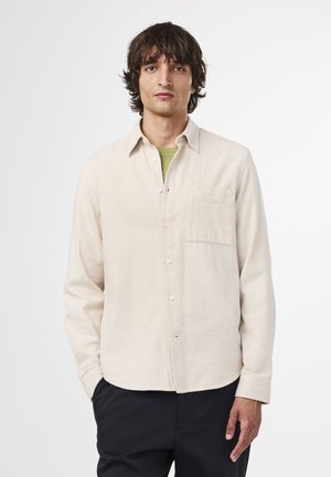 Beige skjorta med knappar i texturerat tyg, en bröstficka och krage. Bärs över en grön skjorta med långa ärmar.