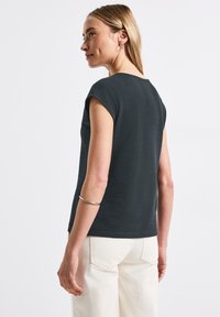 Mörkgrå texturerad kortärmad topp med rund halsringning, bärs med ljusa byxor. Har en avslappnad passform och subtila sömnadsdetaljer.