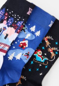 Três pares de meias de lã com padrões de inverno: paisagem urbana nevada, cena de floresta festiva e Pai Natal com renas. As cores incluem azul, preto e branco.