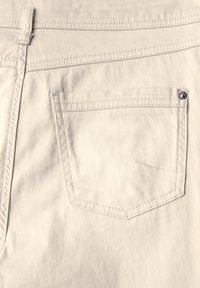 Bermudas blancas de algodón con un bolsillo trasero que presenta costuras en contraste y un detalle de botón de metal. Textura suave, diseño minimalista.