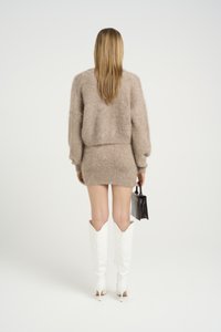 Beige fluffy cropped genser og tettsittende miniskjørt, kombinert med hvite knähøye støvler og holder en liten svart håndveske.