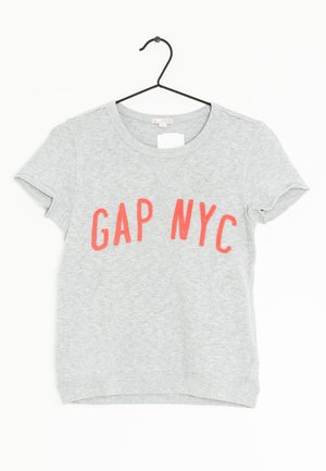 T-shirt gris à manches courtes suspendu à un crochet noir, arborant un imprimé corail "GAP NYC" sur le devant. Tissu doux, design décontracté.