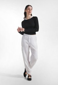 Schwarzes, geripptes Langarmshirt, weiße Cargo-Hose mit Taschen und schwarze Ballerinas. Weiche Texturen, figurbetontes Oberteil und entspannte Hosen-Silhouette.