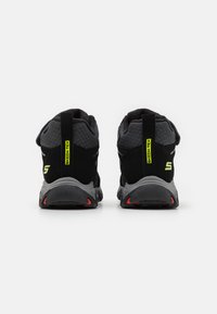 Scarpe da ginnastica nere con accenti grigi, tessuto in rete, tacco resistente, dettagli riflettenti e suola ammortizzata con evidenziature rosse.