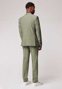 Jasnozielony garnitur o teksturowanym wykończeniu. Dopasowana marynarka z pojedynczym rozcięciem z tyłu, w zestawie z pasującymi spodniami. Białe sneakersy.