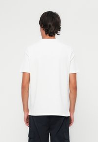 White cotton t-shirt with short sleeves and a round neckline, visible seam details at the shoulders, worn with dark cargo shorts.