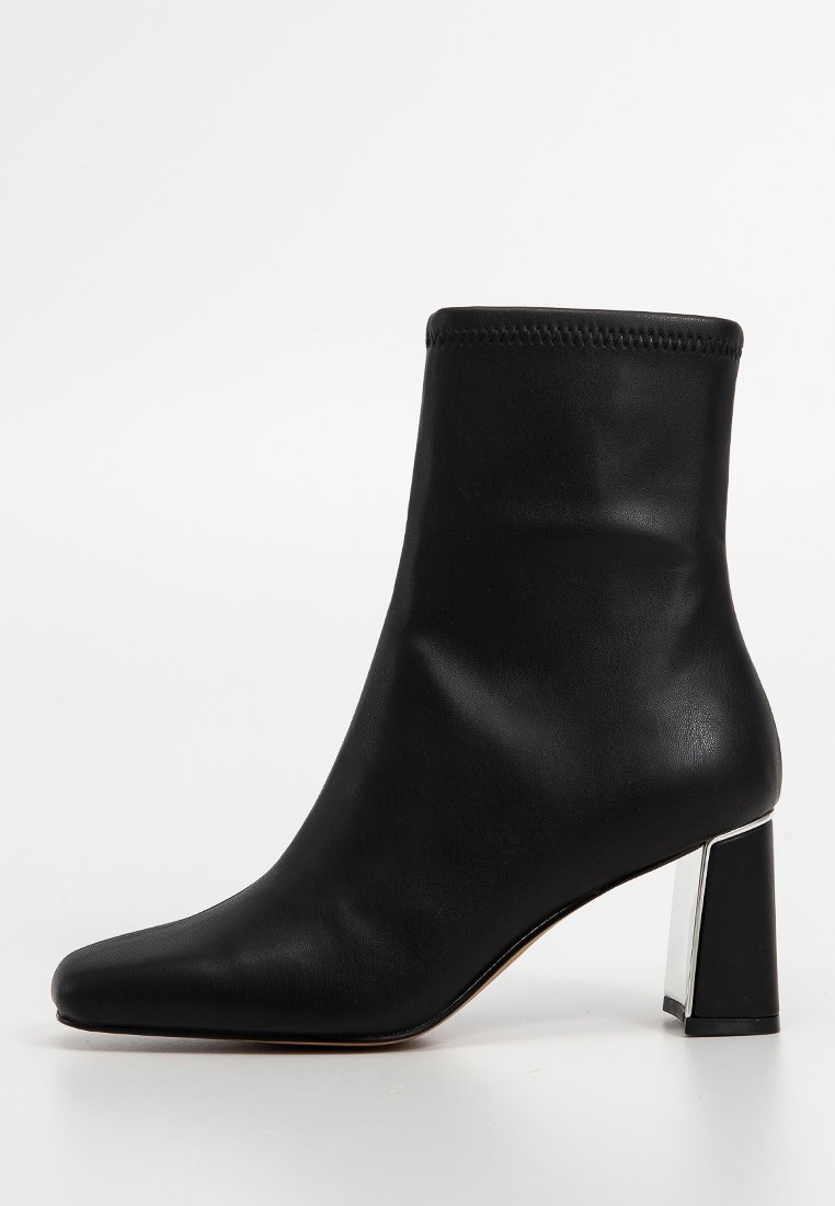 Botín negro de cuero suave con punta afilada y tacón metálico cuadrado. Presenta un ajuste ceñido en el tobillo con costuras mínimas.