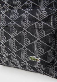 Fekete farmer hátizsák fehér geometrikus mintával, texturált felülettel, zöld és fehér hímzett krokodil logóval.