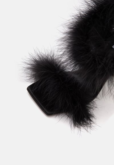 Chaussure à talon haut noire avec bout carré et garniture de plumes noires duveteuses autour de la cheville et des zones des orteils sur fond blanc.