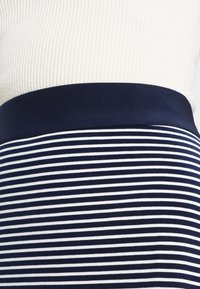 Navy ja valge triibuline seelik, millel on kindel navy vöökoht. Kanga pind näib sile ja kergelt, mis on mõeldud mugavaks istuvuseks.