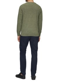 Zielony sweter z dzianiny o teksturowanym wzorze, okrągłym dekolcie i długich rękawach, w zestawieniu z granatowymi spodniami i czarnymi butami.