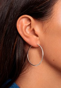 Zilveren ring oorbel, cirkelvormig, dun ontwerp, hoogglanzende afwerking, bevestigd aan een geperforeerd oor. Haar gedeeltelijk zichtbaar.