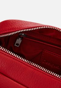 Innenraum einer roten Ledertasche mit einem Reißverschlussfach. Verfügt über einen silbernen Reißverschluss, ein Stofffutter und ein geprägtes Logo-Patch. Strukturiert Oberfläche sichtbar.