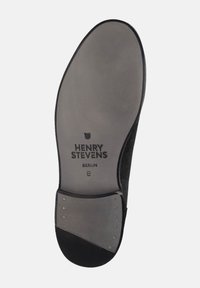 Zwarte suede schoenzool met een textuur van grijs rubber, met het reliëf merkname "HENRY STEVENS BERLIN" en metallic accenten nabij de hak.