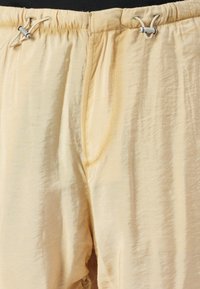 Beige lette shorts med elastisk midje og hvite snøre sikret med små sylinderformede låser.