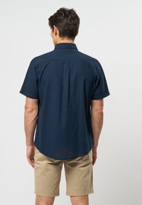 Marinblus med kort ärm, ryggsöm, avslappnad passform, texturerad tyg och rundad fåll, matchad med beiga shorts.