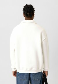 Witte oversized sweatshirt met een kraag, geribde manchetten en zoom. Gemaakt van katoen, met een soepele textuur, getoond vanuit de achterkant tegen een neutrale achtergrond.