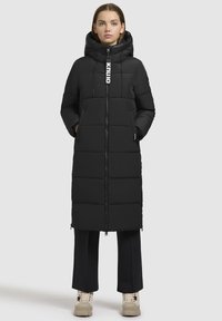 Polstret sort lang jakke med hætte, med lynlåslukning, sidelommer og justerbar snor. Glat tekstur og firkantet design.