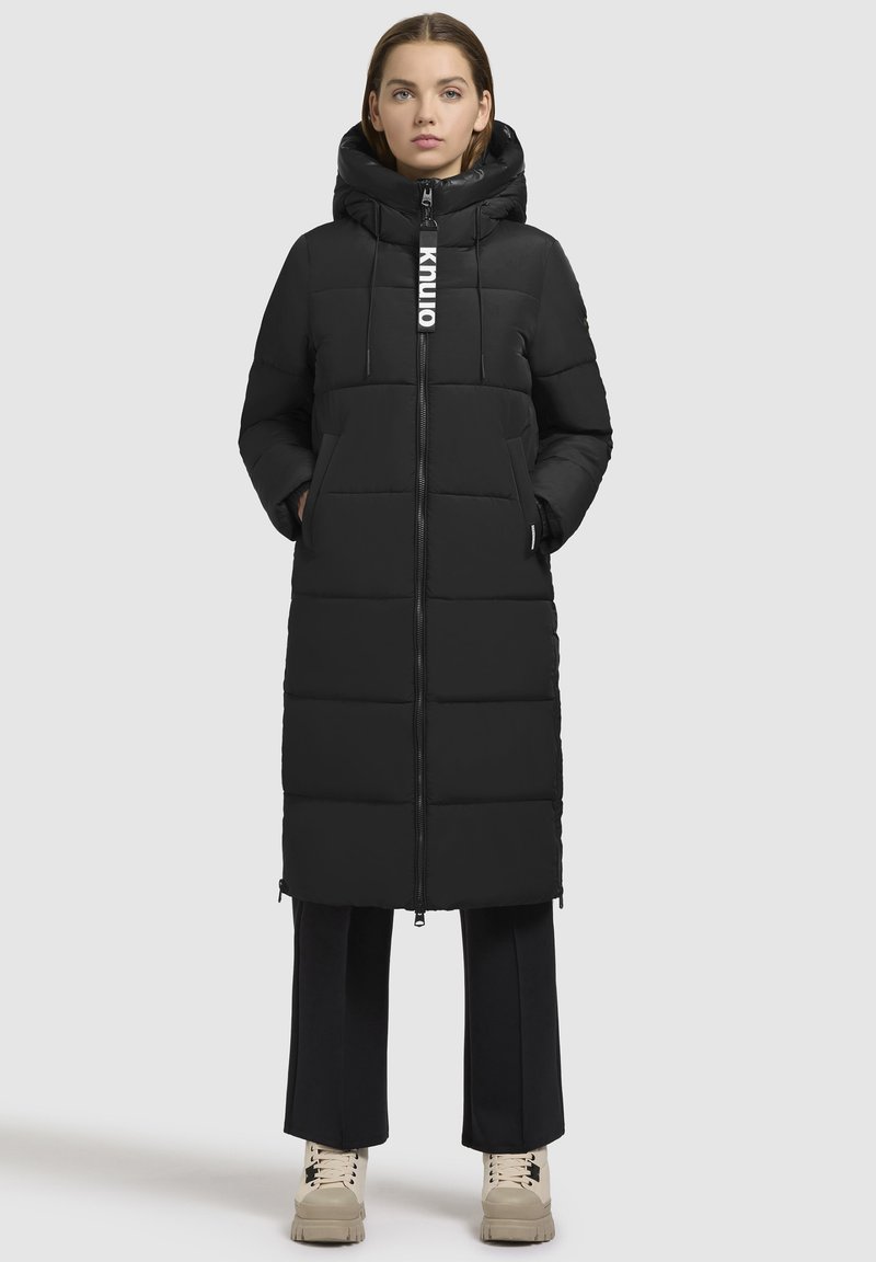 Polstret sort lang jakke med hætte, med lynlåslukning, sidelommer og justerbar snor. Glat tekstur og firkantet design.