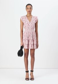 Βραχυνμένο ροζ φόρεμα με λουλούδια, ελαστική μέση, φουσκωτά μανίκια και φουσκωτό φούστα. Μοντέλο κρατώντας μια μικρή μαύρη τσάντα, φορώντας μαύρες γόβες.