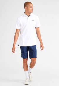 Polo blanc avec un col gris, associé à un short bleu marine. La tenue présente des manches courtes et un logo discret sur la poitrine.