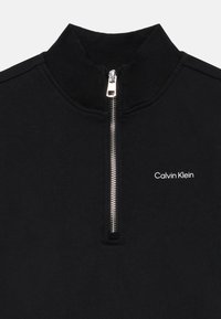 Čierna mikina na zips vyrobená z bavlnenej zmesi. Obsahuje vysoký golier, kovový zips a vyšívané logo "Calvin Klein" na hrudi.
