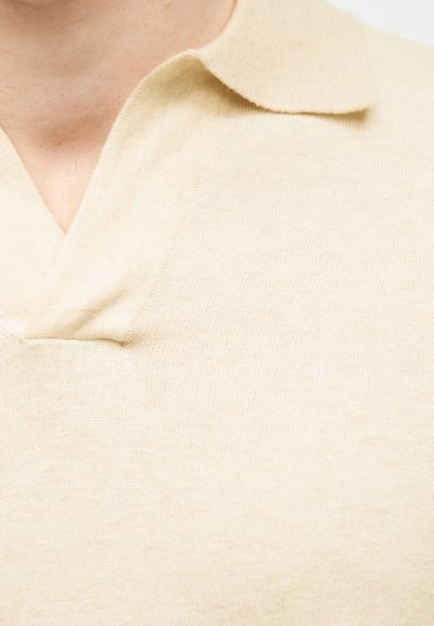 Πλεκτό πόλο σε κρεμ χρώμα με απαλό γιακά στο πάνω μέρος του στήθους και του λαιμού ενός ατόμου.