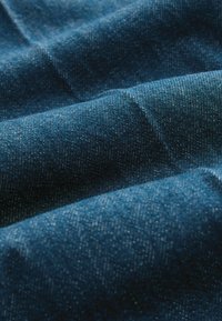 Gros plan d'un tissu denim bleu plié montrant la texture et les détails du tissage avec des reflets et des ombres subtils.