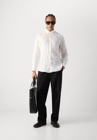 Chemise en lin blanche, pantalons larges noirs, sac en cuir noir et lunettes de soleil noires. Design simple avec une coupe décontractée et un contraste de textures.